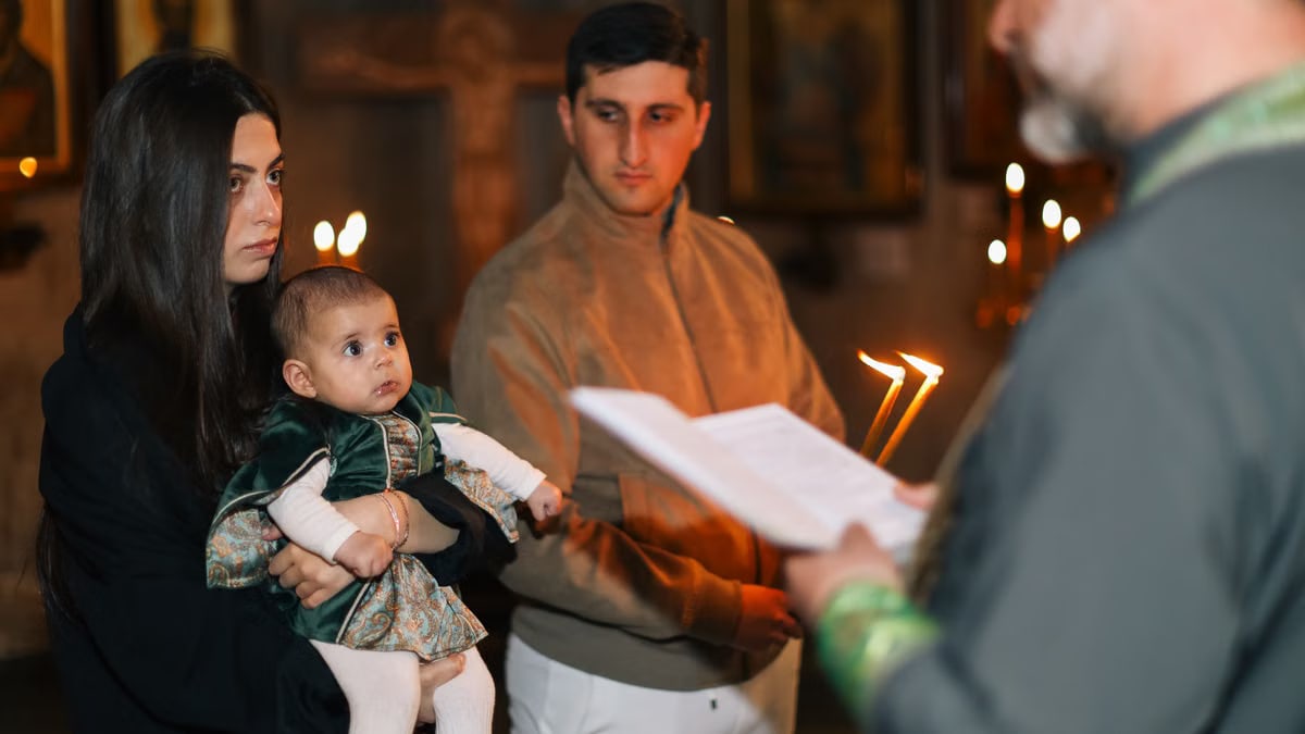 A family participates in a traditional religious ceremony with candlelight indoors.